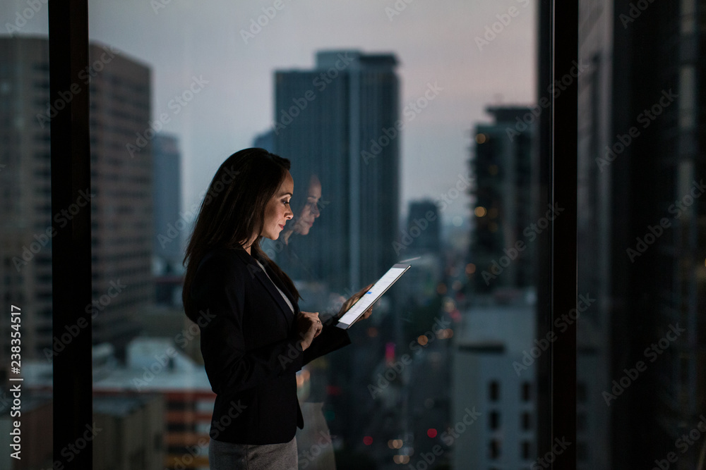 Businesswoman working late using digital tablet with city skyline in background